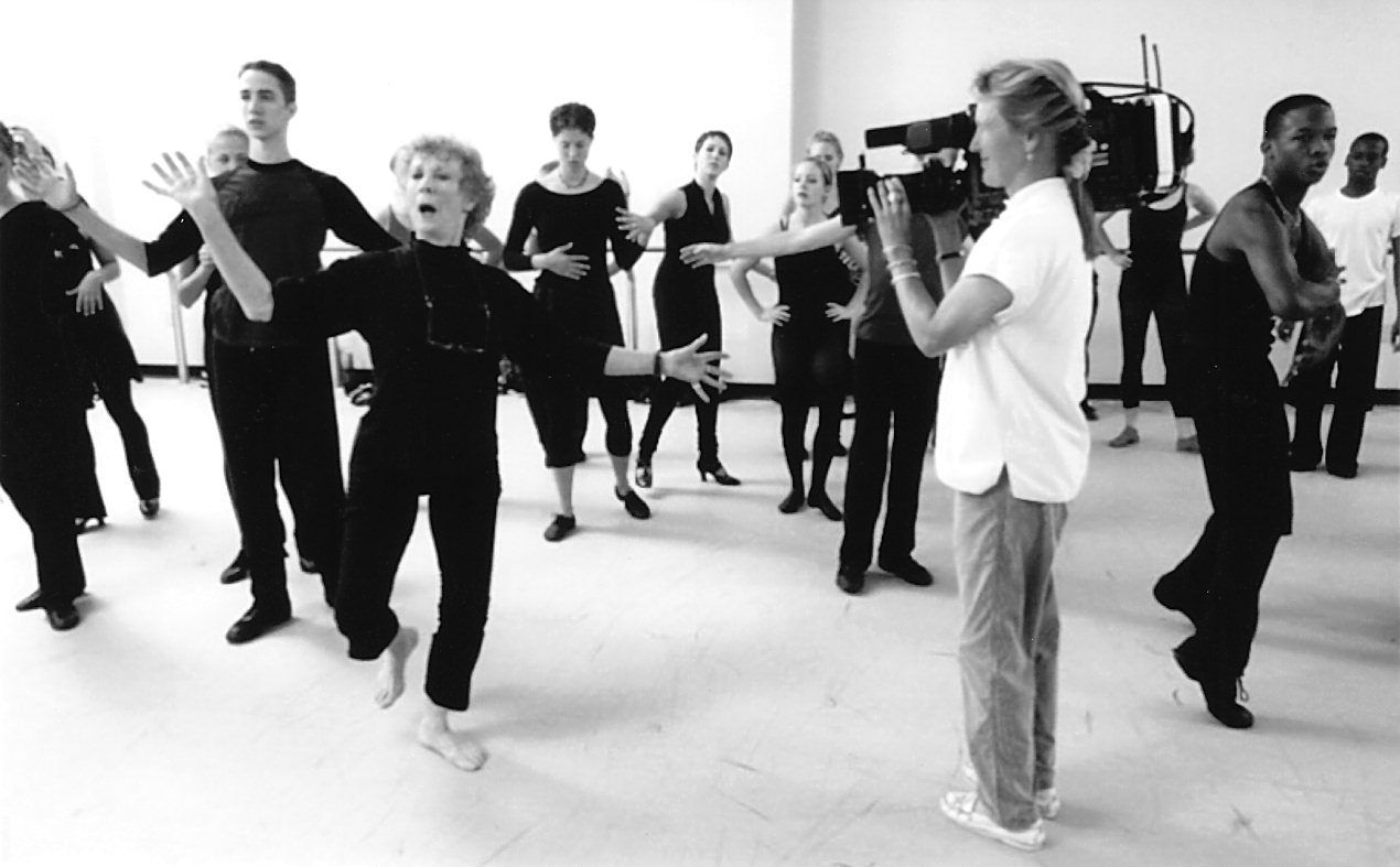 Dance rehearsal with camerawoman filming performers.