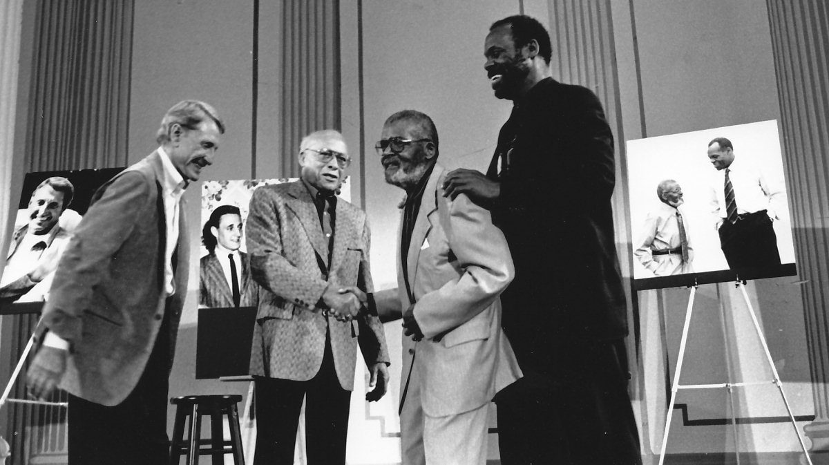 Four men smiling and shaking hands.